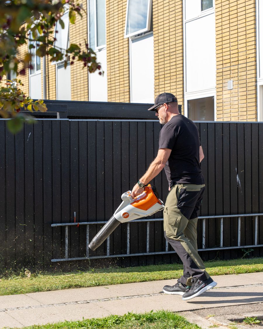 Gartner rydder op med løvblæser langs et hegn