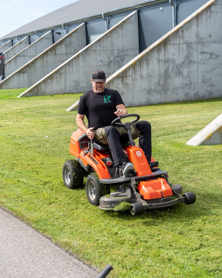 Gartner fra RobinHave klipper græs med havetraktor på en grøn skråning